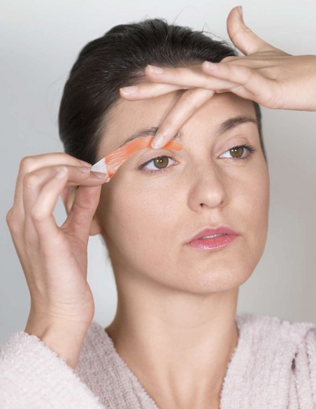 Donna che applica una striscia depilatoria per sopracciglia sotto al suo sopracciglio Donna che applica una striscia depilatoria per sopracciglia sotto al suo sopracciglio